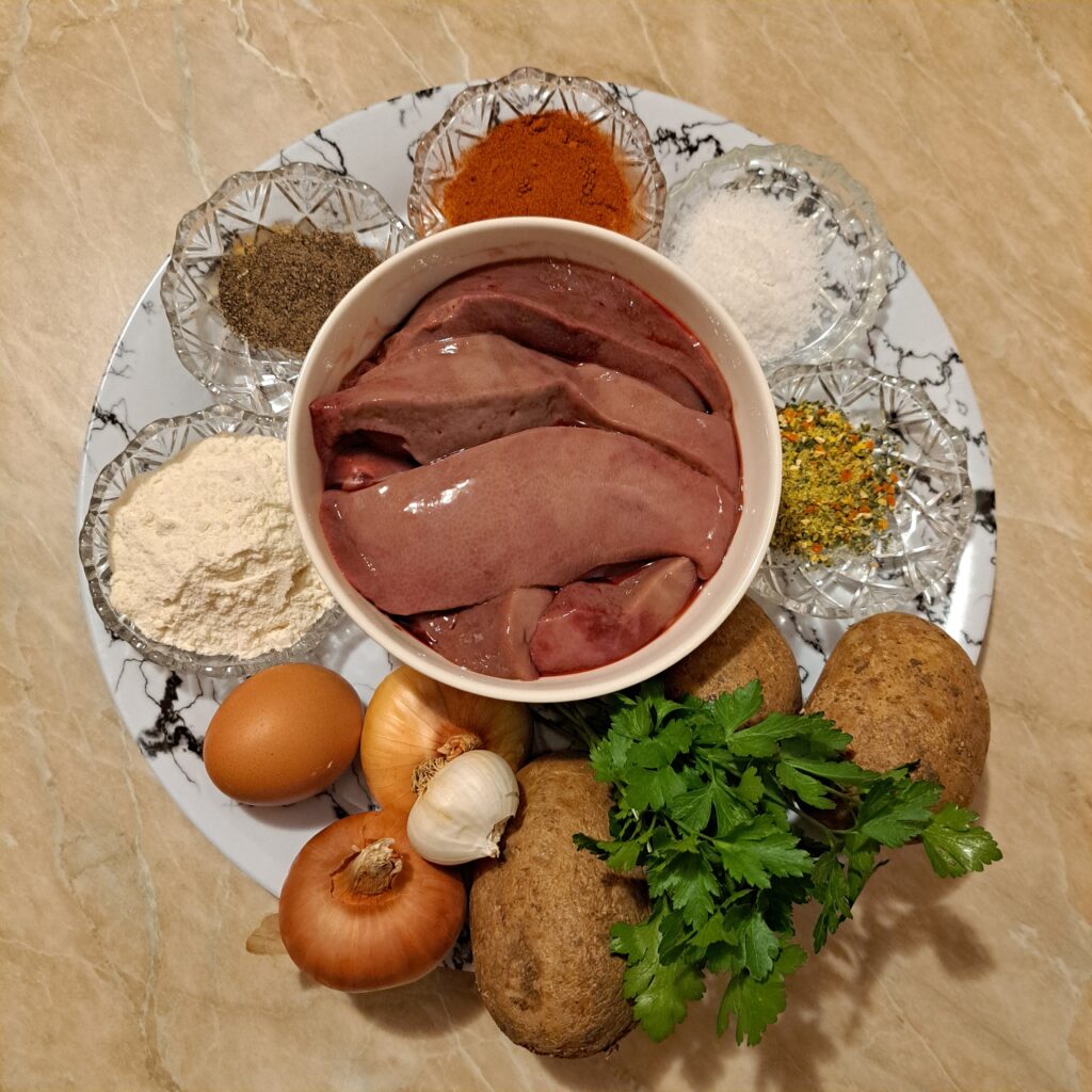 All ingredients placed on a wide flat plate, including pork liver, potatoes, onion, garlic, parsley, egg, flour, and spices.