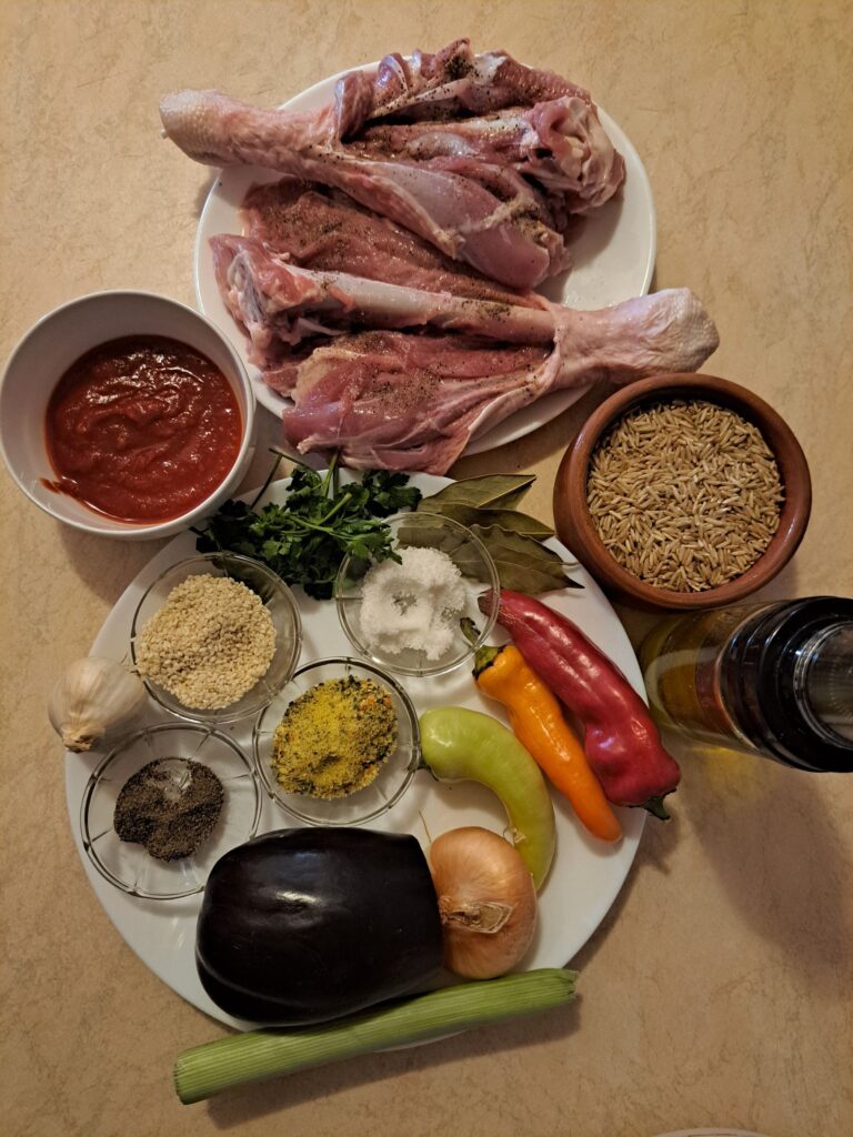 Fresh ingredients for Turkey Drumsticks Veggie Rice arranged on a kitchen table, including turkey drumsticks, brown rice, vegetables, garlic, and spices.