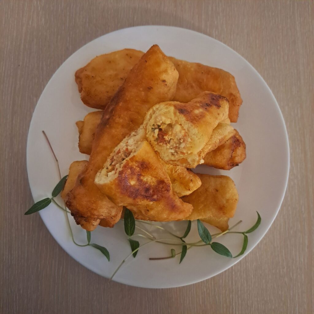 Plate with Cheesy Sujuk Stuffed Piroshki decorated with a few microgreens, with one cut piroshka showing its soft filling.