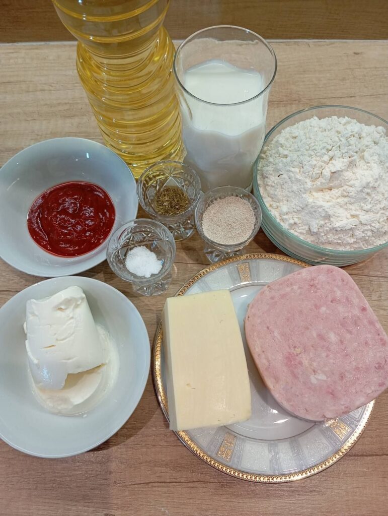 Top view of all ingredients for Fried Folded Ham Pizzas arranged on a kitchen table, ready for preparation.