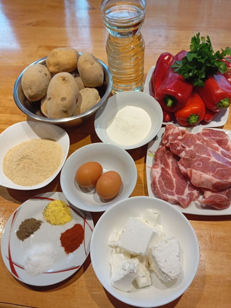 Boneless pork neck medallions, red peppers, potatoes, feta cheese, eggs, flour, breadcrumbs, and spices arranged on a kitchen counter.