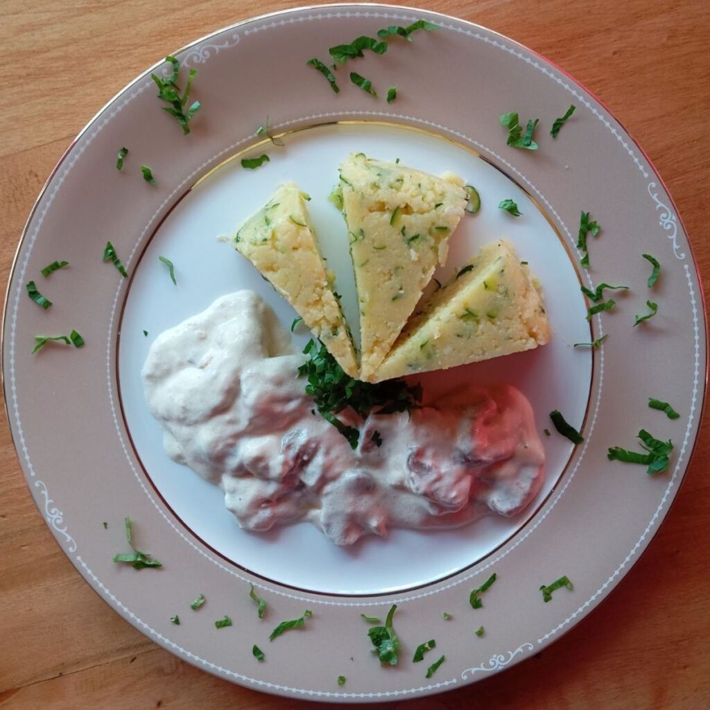 A single plate serving of Pork Sauce Zucchini Polenta with a quarter of polenta, pork and mushroom cream sauce, and sprinkled fresh parsley.