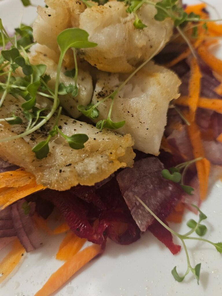 Pan-seared white fish served with colorful beet and carrot slaw on a plate, close-up view.