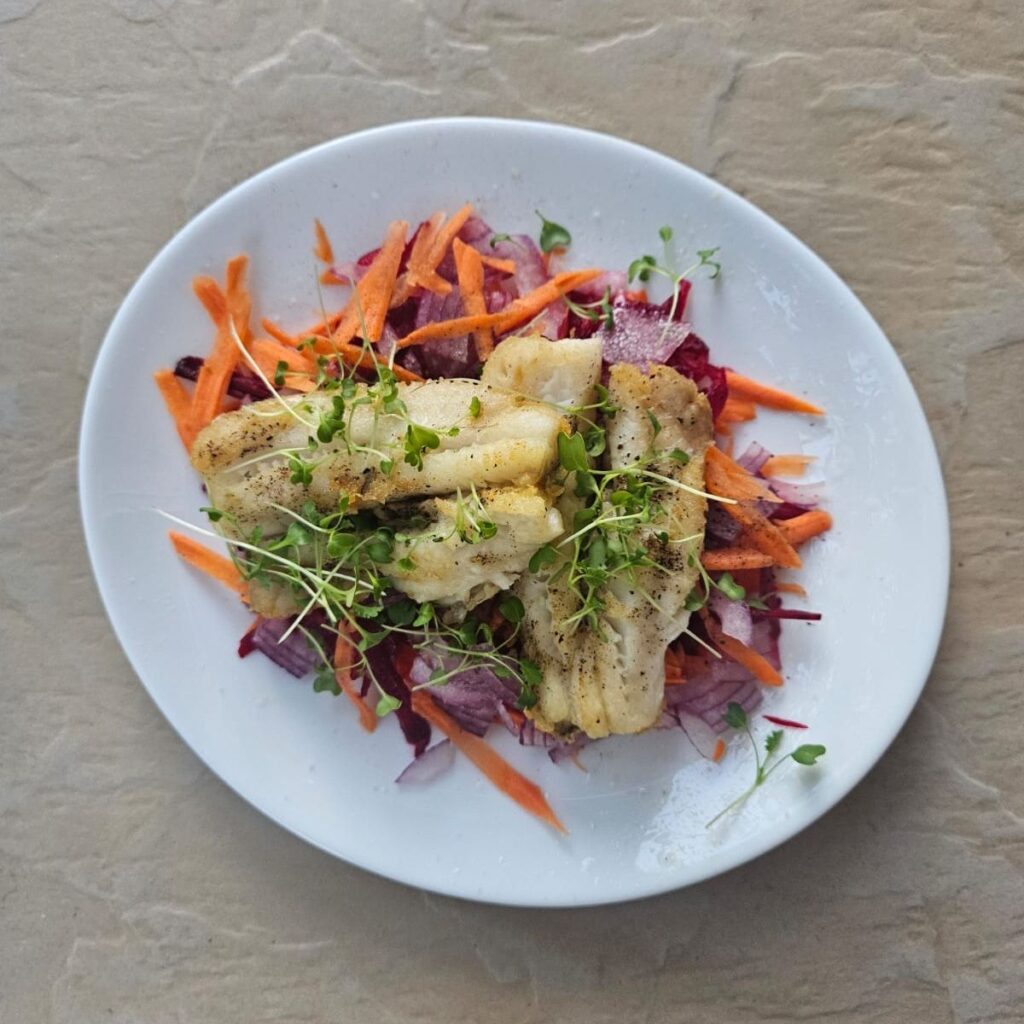 Pan-seared white fish with beet and carrot slaw, beautifully plated and garnished with microgreens.