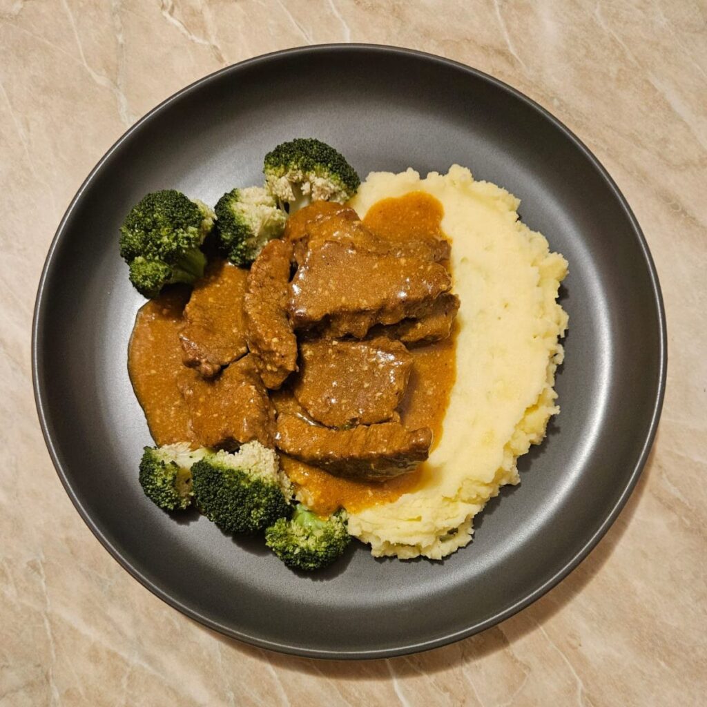 Beef Gravy with Mashed Potatoes and Broccoli beautifully arranged on a plate, with tender beef in rich brown sauce beside creamy mash and bright green broccoli florets.
