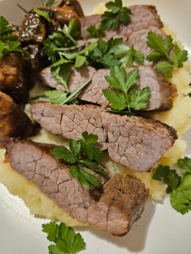 Close-up of sliced pan-seared beef on creamy potato mash with sautéed mushrooms.