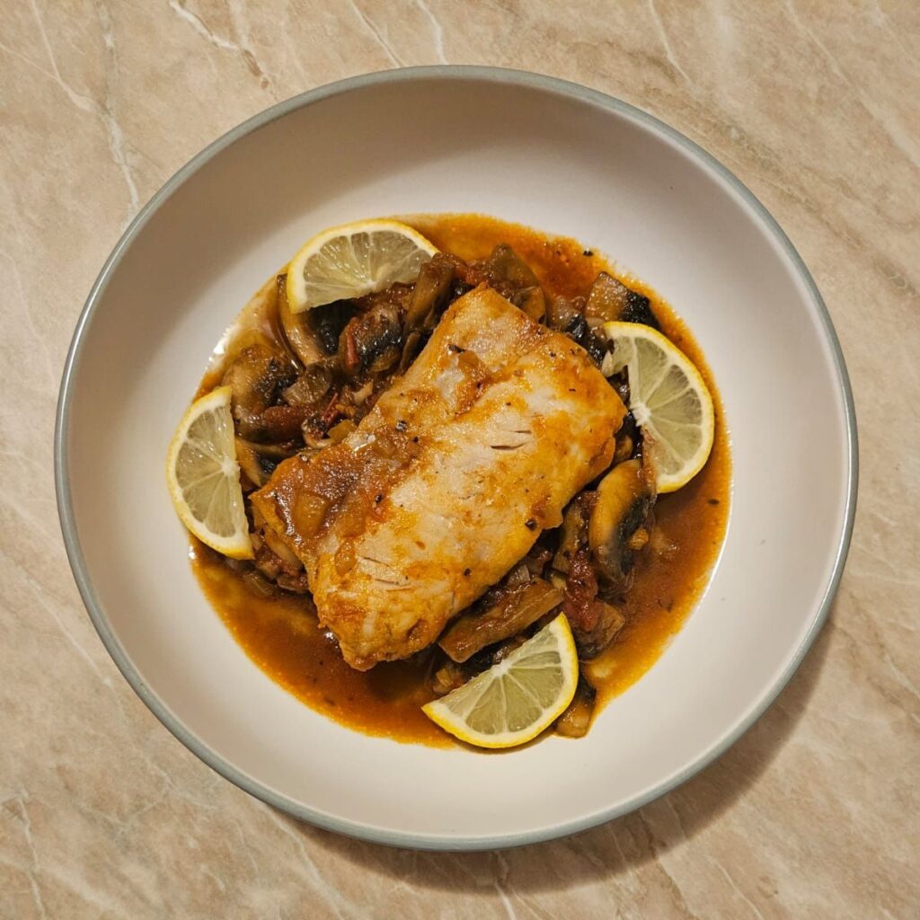Fish Stew with Tomato and Mushrooms served in a shallow plate, garnished with parsley and lemon slices.