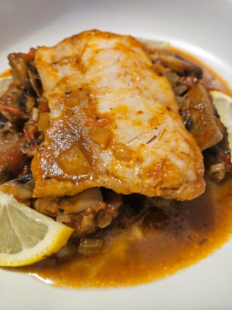 Close-up of a delicious fish stew with tomatoes, mushrooms, and herbs.