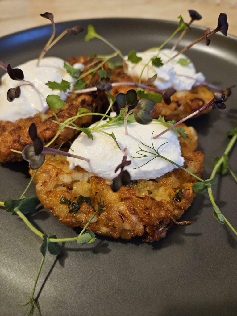 Three millet patties topped with Greek yogurt and decorated with fresh microgreens on a plate.
