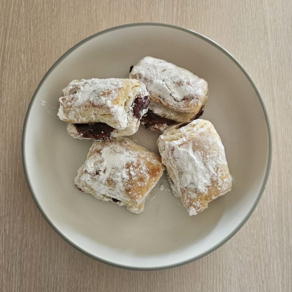 A plate with four Flaky Lard Homemade Pastries, coated in powdered sugar, ready to enjoy.