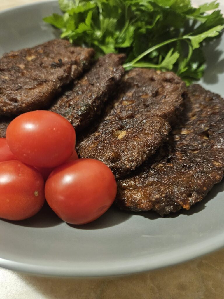 Four Pork Liver Potato Patties served on a plate with cherry tomatoes and a small bunch of parsley.