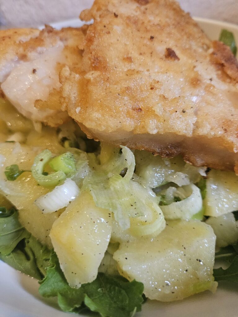 Close-up of a single serving of Fried Pangasius Potato Salad on a plate with arugula, crispy fillets, and fresh potato salad.