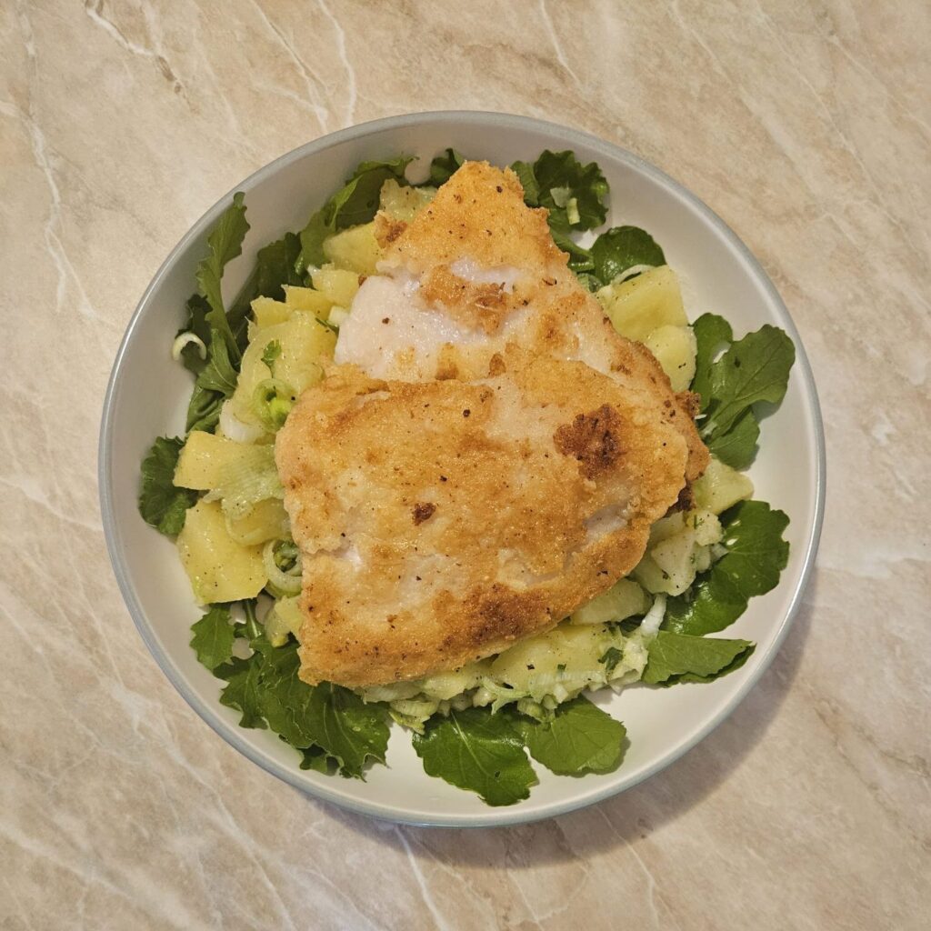 Fried Pangasius Potato Salad served on a plate with arugula, potato salad in the center, and two crispy Pangasius fillets on top.