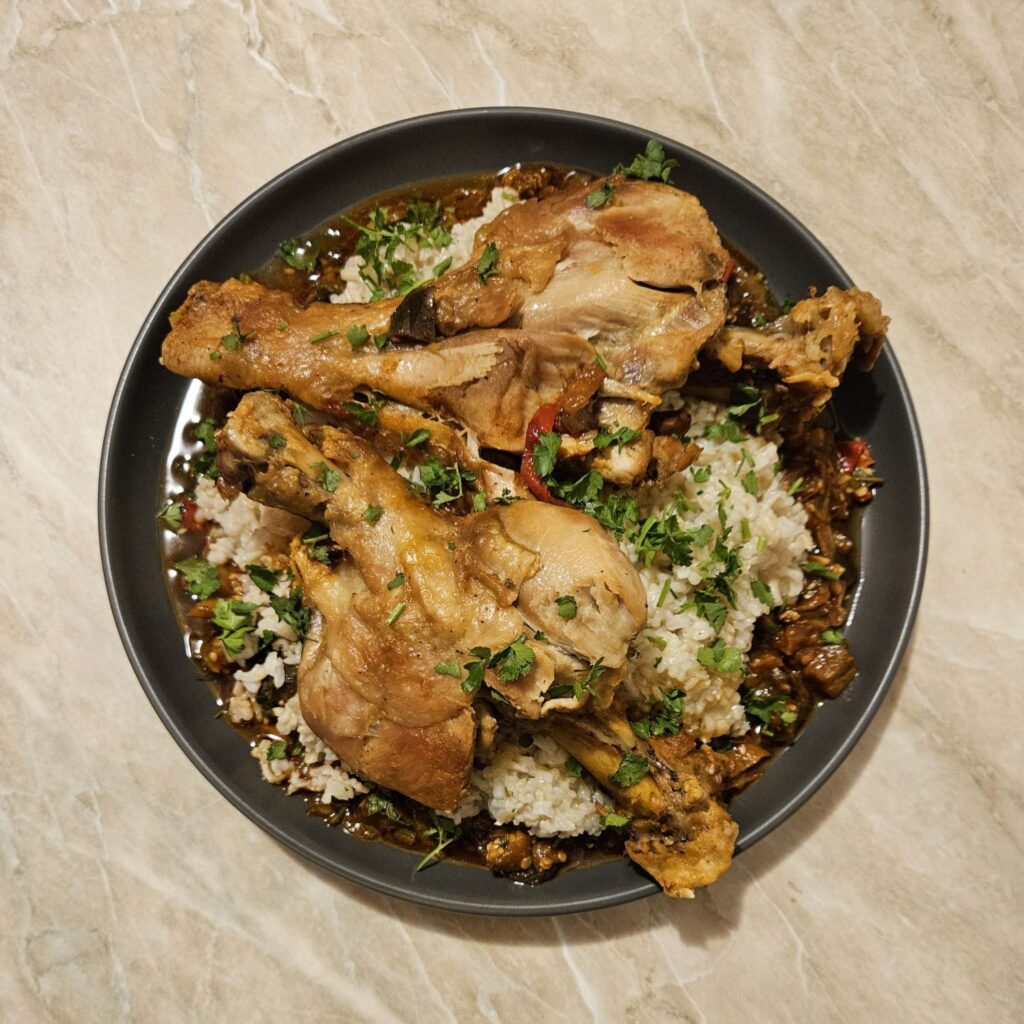 Turkey Drumsticks Veggie Rice served on a flat plate with vegetable sauce at the bottom, brown rice in the middle, and drumsticks arranged on top.
