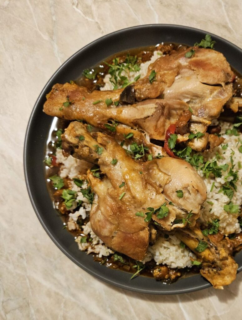 A plate of Turkey Drumsticks Veggie Rice with colorful vegetable sauce and brown rice, garnished with parsley.