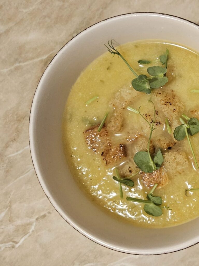 A single serving of Cauliflower Leek Carrot Soup in a small bowl topped with pea microgreens.