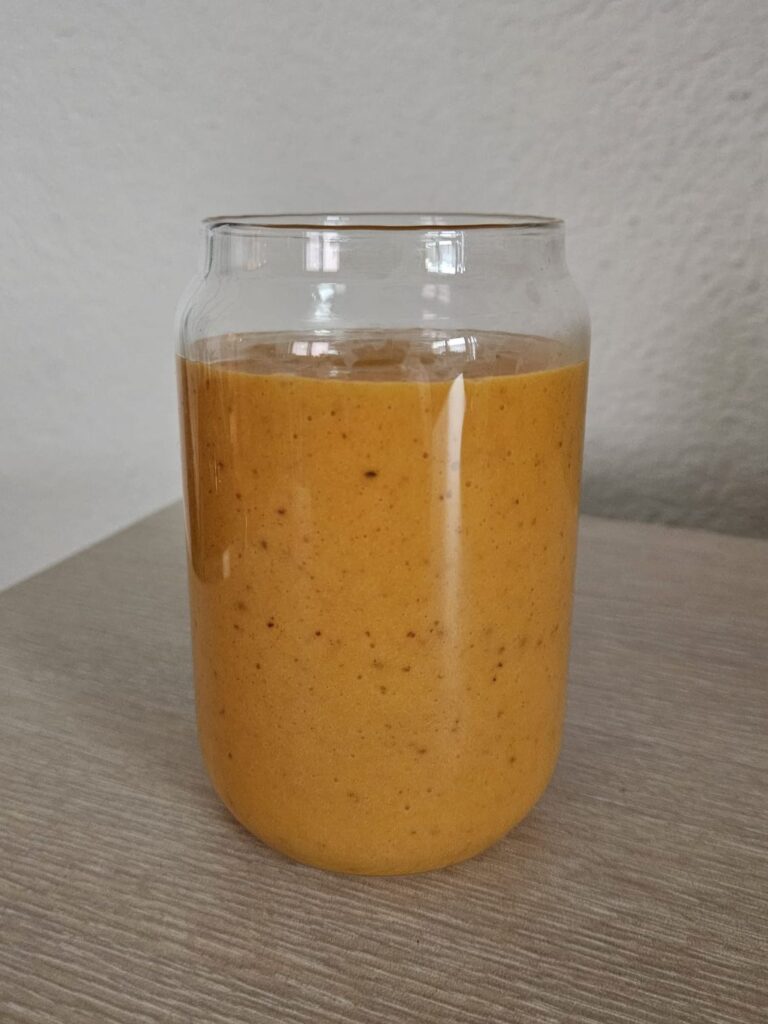 Smoothie made from persimmon, butternut squash, and dried cranberries, served in a clear glass with soft orange color.