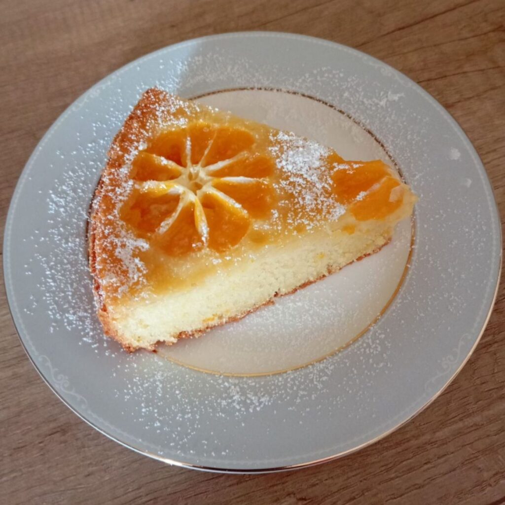 A close-up of a simple juicy mandarin cake slice served on a plate, showing its soft texture and glossy fruit layer.