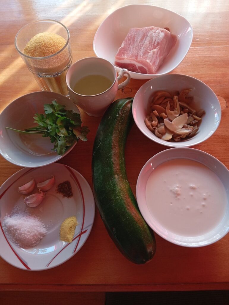 All ingredients for Pork Sauce Zucchini Polenta arranged on a kitchen table, including polenta, pork, mushrooms, zucchini, garlic, cooking cream, parsley, and seasonings.