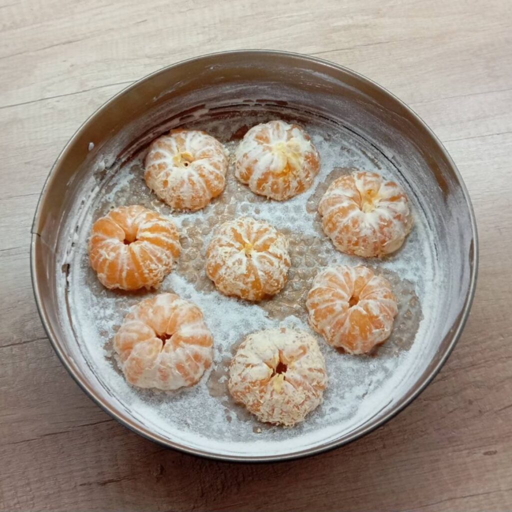 Halved mandarins neatly arranged in the greased baking pan, ready for batter.