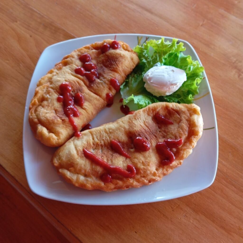Two Fried Folded Ham Pizzas served on a plate with a scoop of sour cream on a green leaf and a drizzle of ketchup on top.