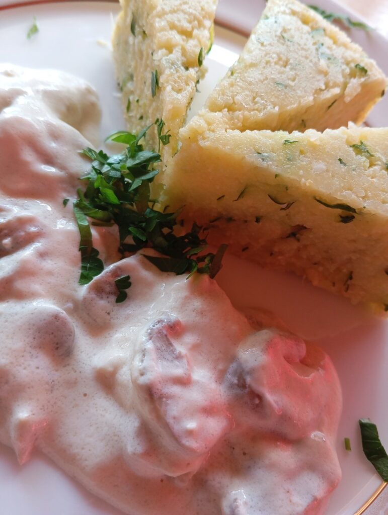Close-up view of zucchini polenta slices served with pork, mushrooms, and cooking cream sauce on a plate.