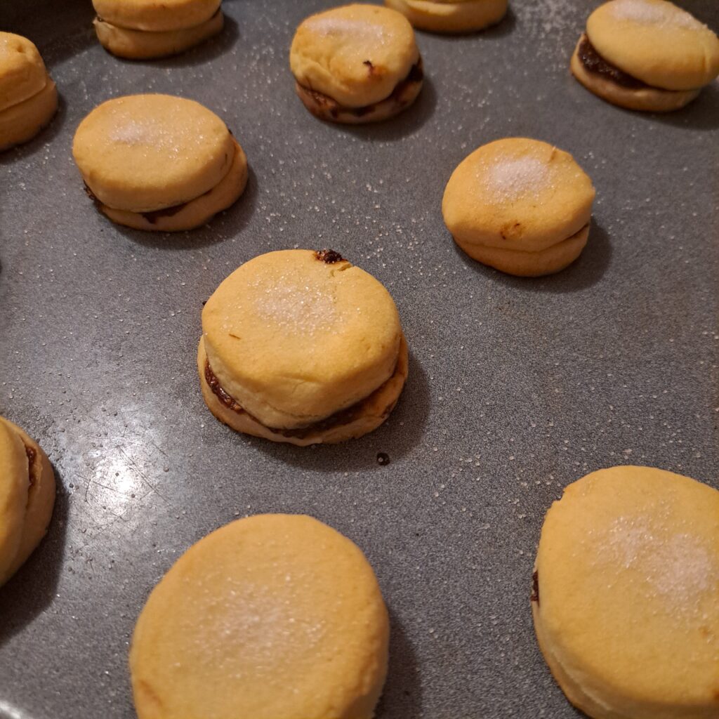 Freshly Baked Jam Sandwich Cookies in a tray, golden and ready to be coated with powdered sugar.