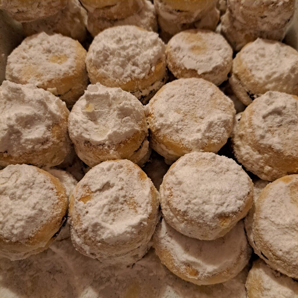 A plate filled with freshly baked jam sandwich cookies coated in powdered sugar, neatly arranged and ready to serve.