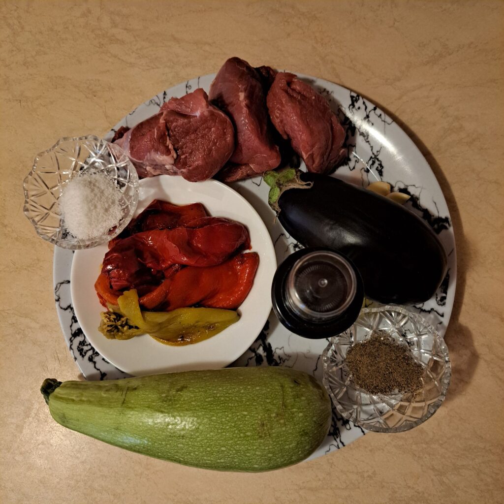 Assorted fresh ingredients for Rustic Beef Veggie Plate, including beef, zucchini, eggplant, peppers, garlic, olive oil, salt, black pepper, and chives, ready for preparation.