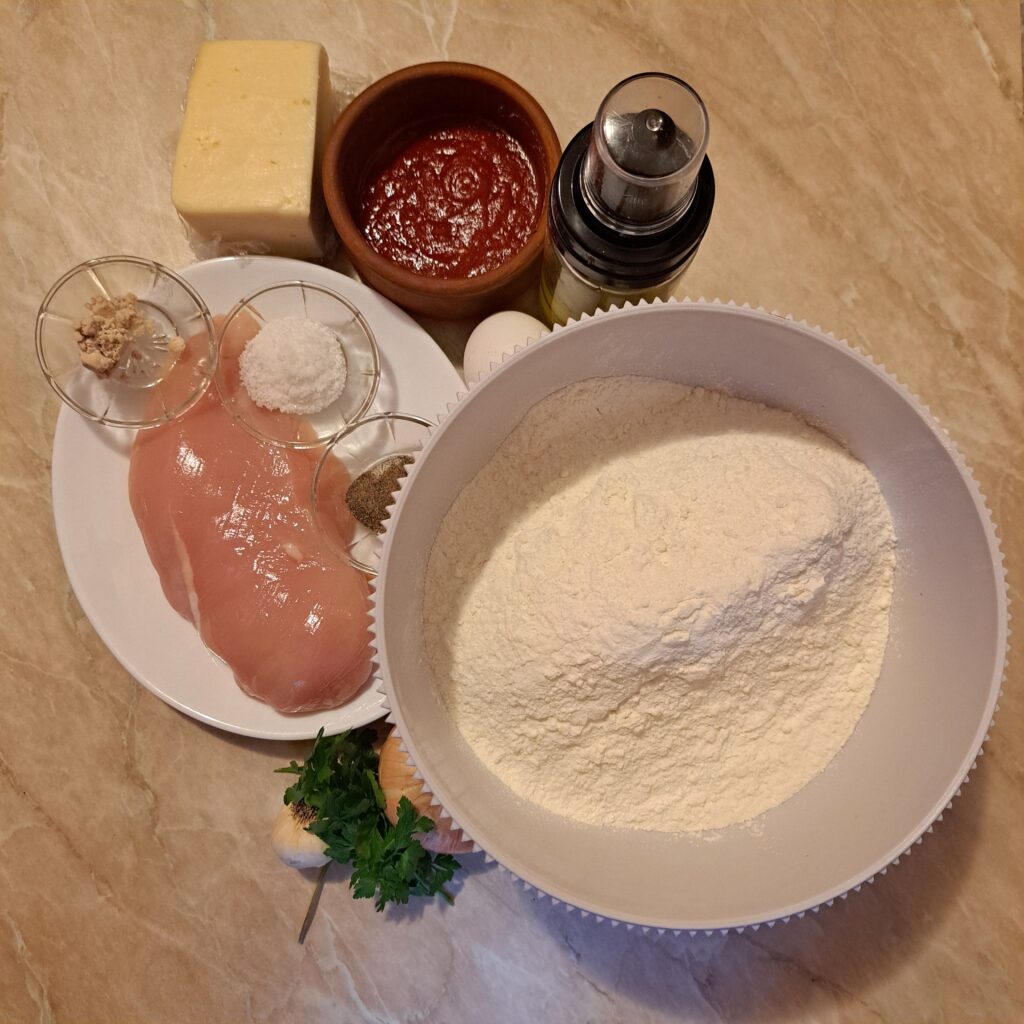 Ingredients for Creamy Chicken Grill Flats including flour, chicken steak, cheese, tomato paste, egg, onion, garlic, olive oil, yeast, salt, pepper, and parsley, arranged neatly on a kitchen countertop.
