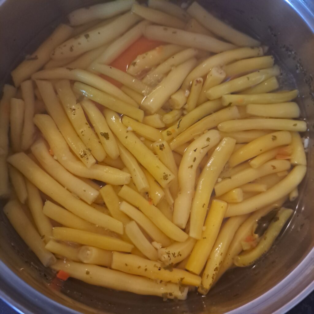 Green beans cooking with sliced carrot in a pot.