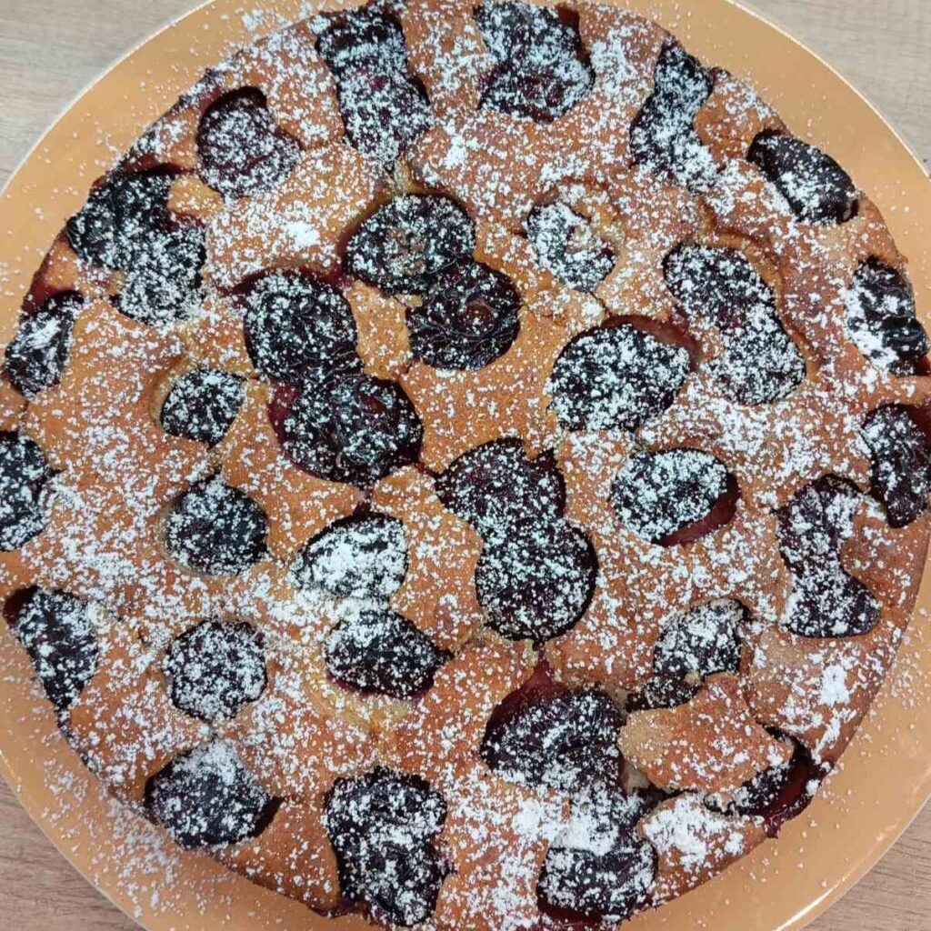The final presentation of our Simple Blue Plum Cake, sprinkled with powdered sugar, highlighting its slightly crisp top and baked plums.