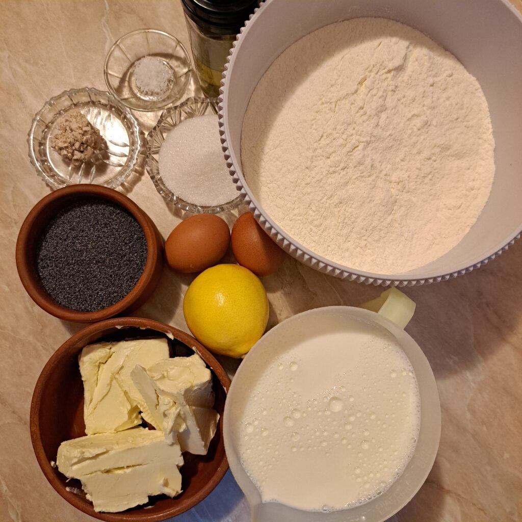 Ingredients arranged on a countertop, including milk, sugar, butter, eggs, yeast, flour, and poppy seeds.