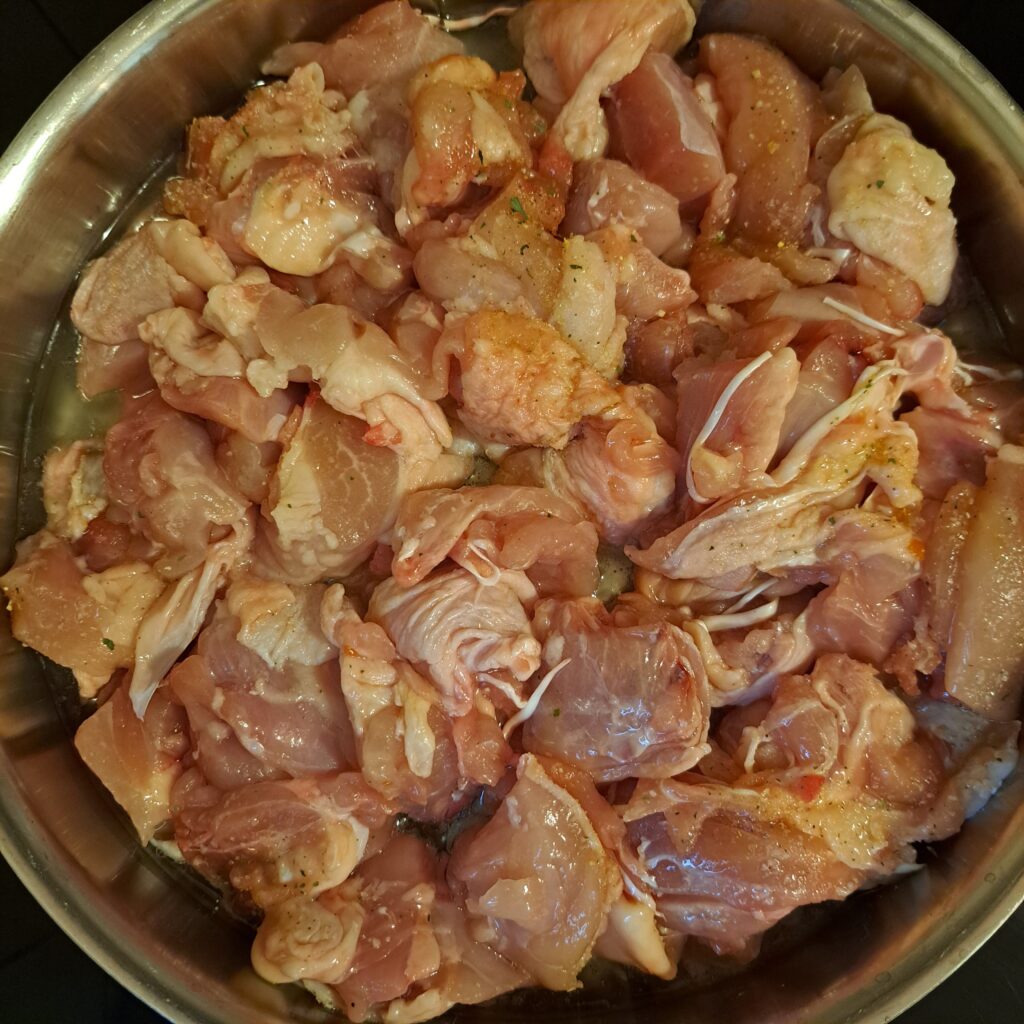 Whole chicken legs cut into bite-sized pieces cooking in a heated pan with oil.