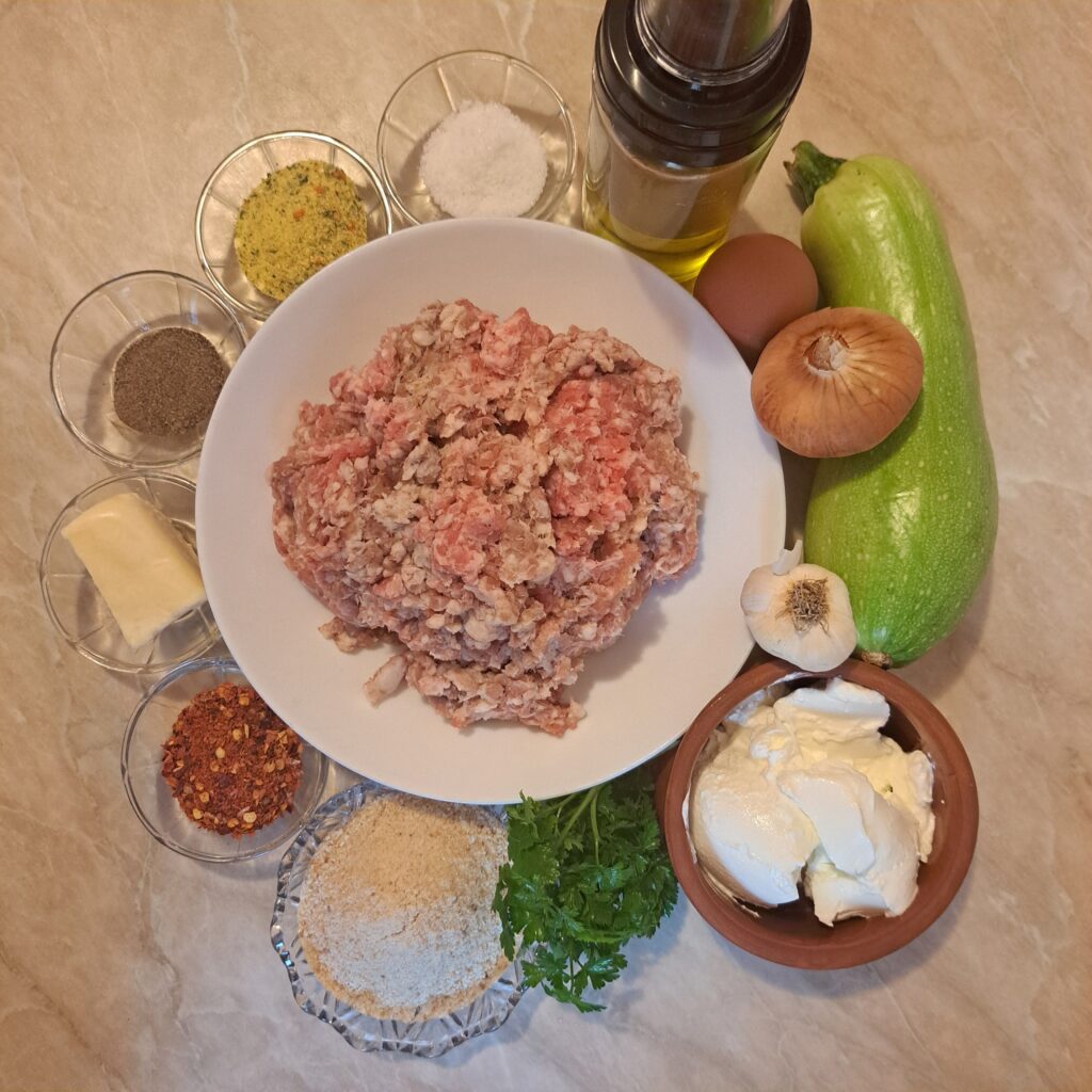 Ingredients arranged on a kitchen surface, including ground meat, cheese, zucchini, sour cream, herbs, and seasonings.