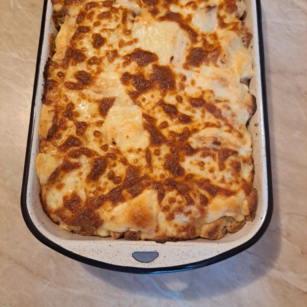 Baked Cheesy Bread Cubes in a baking dish, golden and melted, showing layers of bread, béchamel sauce, hard cheese, kashkaval, and mozzarella.