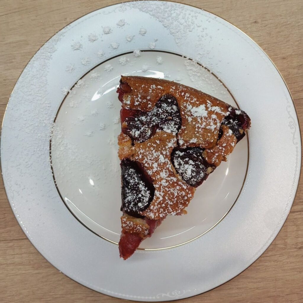 A slice of our Simple Blue Plum Cake on a flat plate, decorated with powdered sugar.