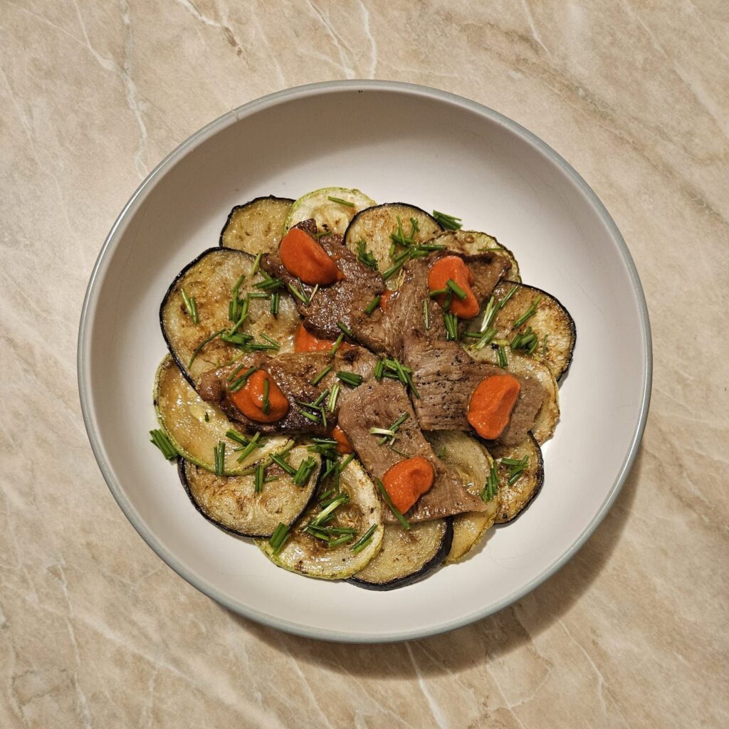 A beautifully arranged Rustic Beef Veggie Plate featuring grilled beef, zucchini, and eggplant rounds with pepper sauce, garnished with fresh chives.