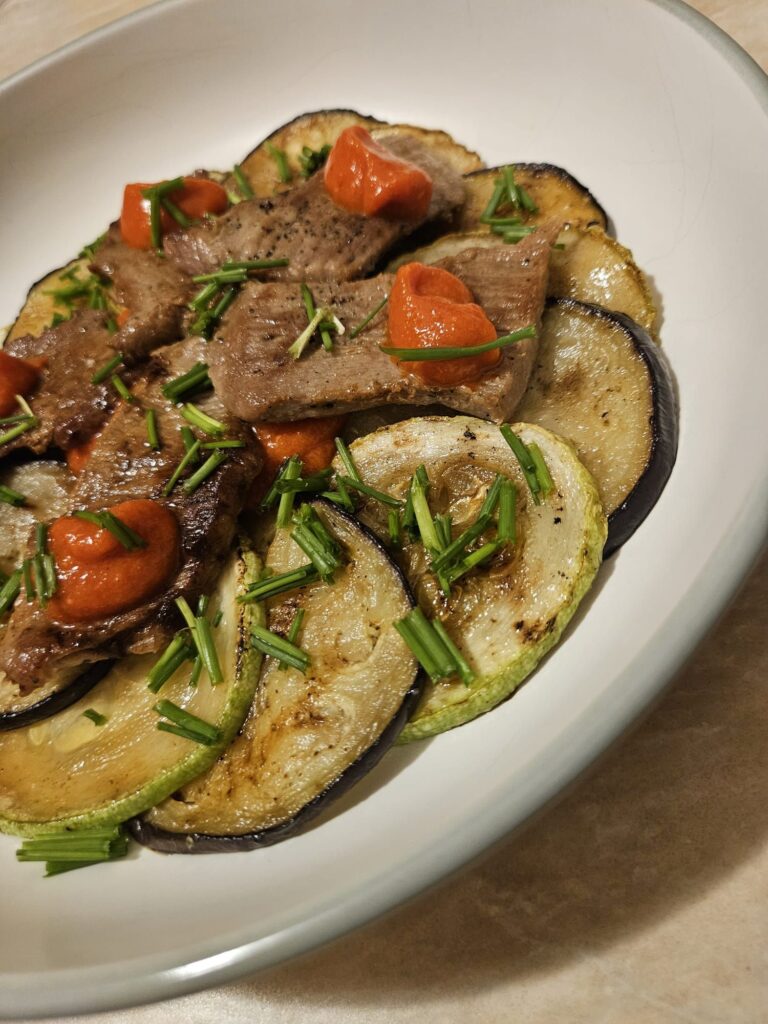 Close-up of a Rustic Beef Veggie Plate with grilled beef, zucchini, eggplant, roasted pepper sauce, and fresh chives, arranged in a circular presentation.