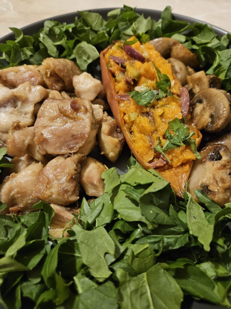 Close-up of a served Juicy Chicken Veggie Plate with juicy chicken pieces, sweet potato filled with chopped olives and pickles, mushrooms, and arugula.