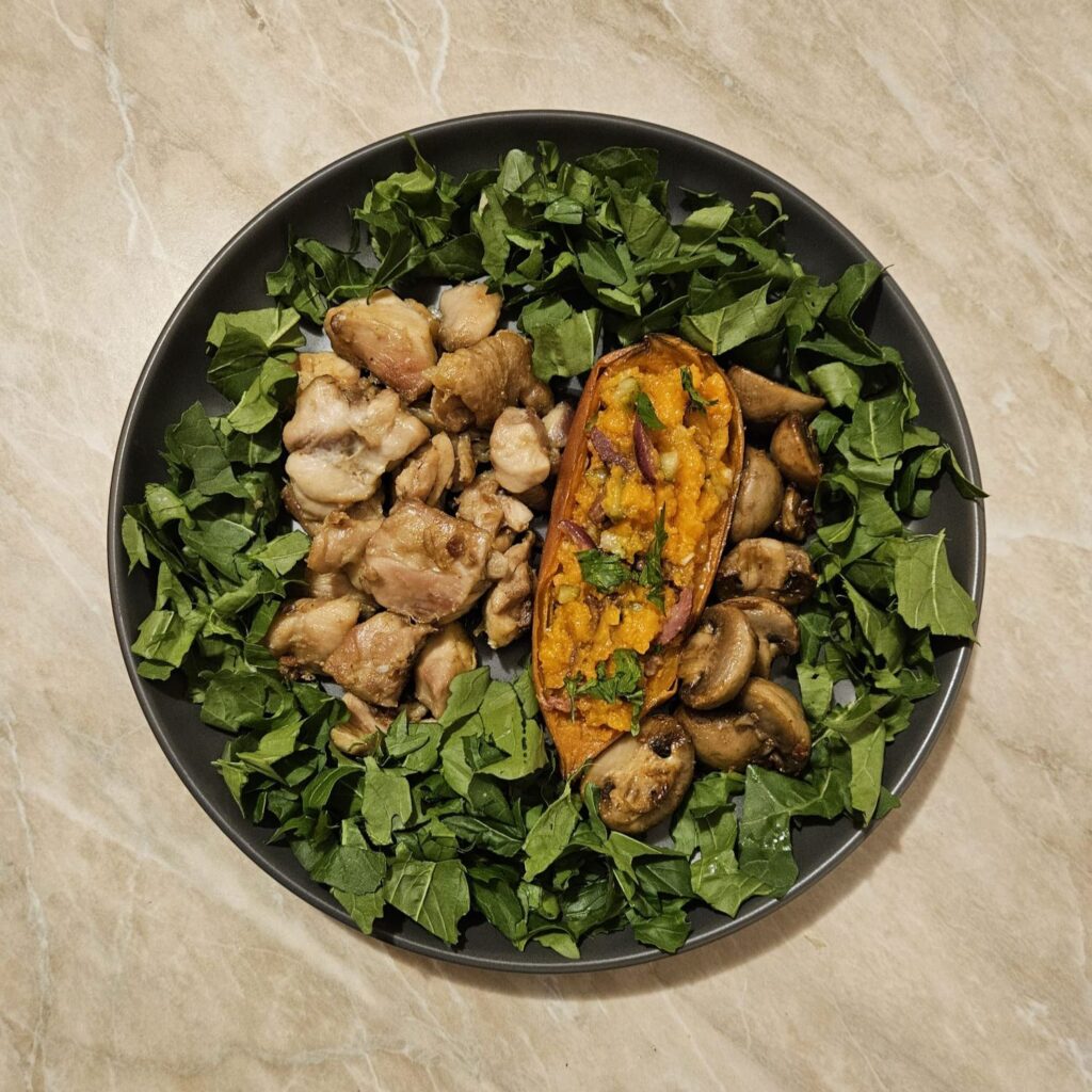A served Juicy Chicken Veggie Plate showing chicken pieces, baked sweet potato filled with olives and pickles, mushrooms, and fresh arugula on the plate.