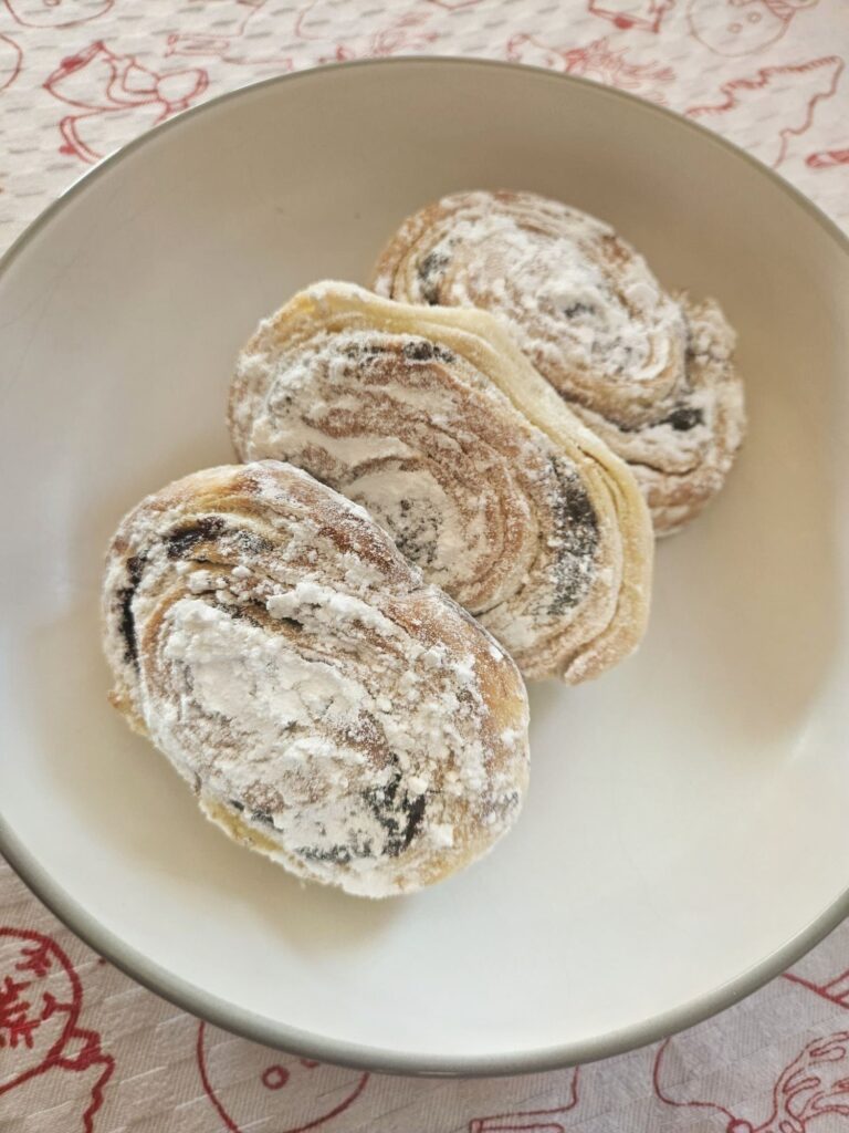 Three flaky poppy seed rolls arranged on a plate, showing soft layers and poppy seed filling in a close-up view.
