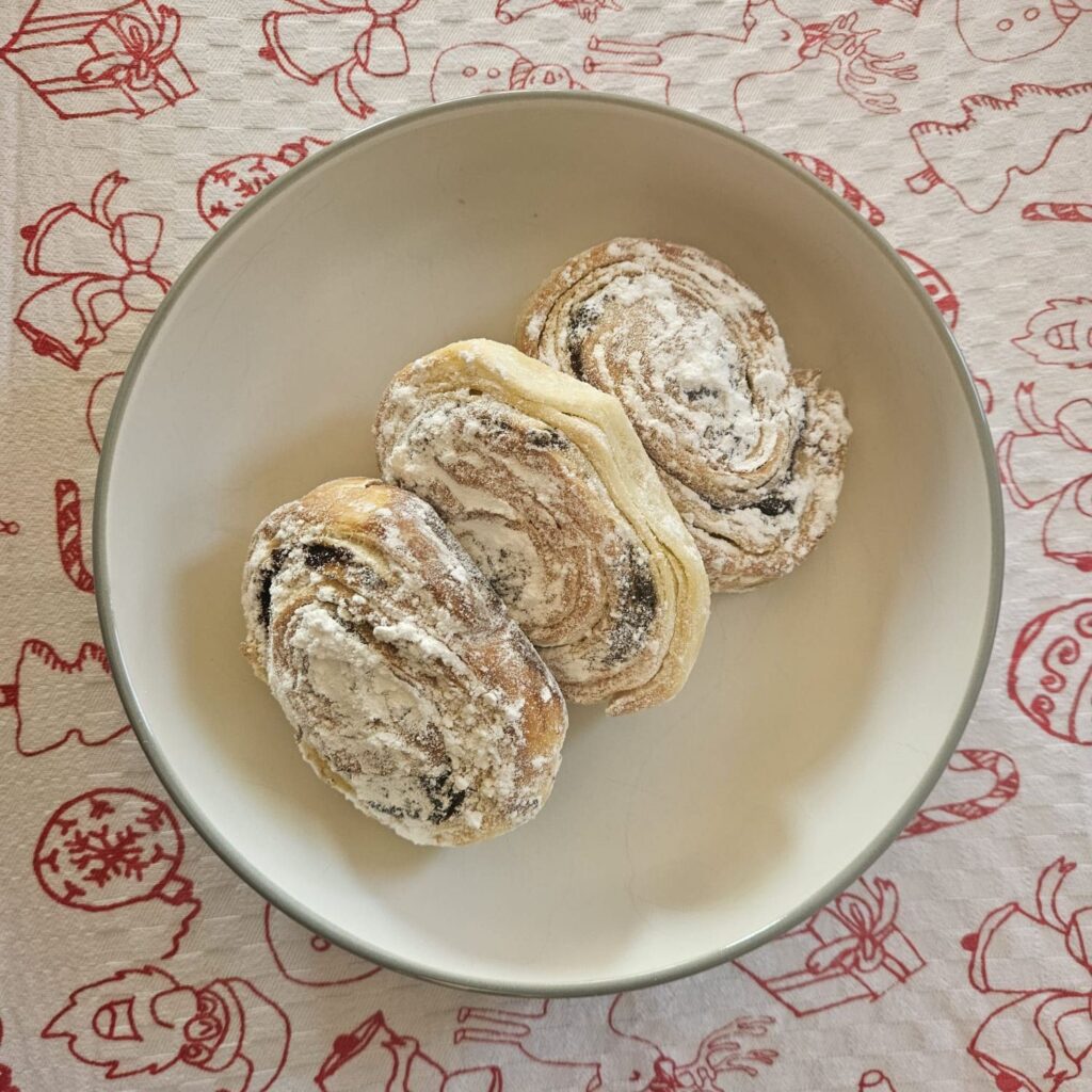 Top view of three Flaky Poppy Seed Rolls arranged on a plate, dusted with powdered sugar.