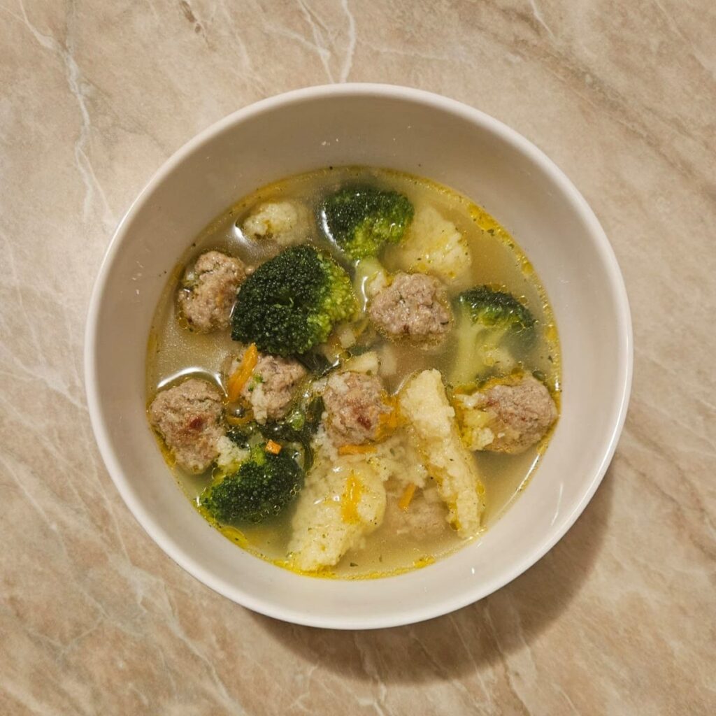 A small bowl of beef meatball dumpling soup, showing meatballs, dumplings, and vegetables in a simple, warm presentation.