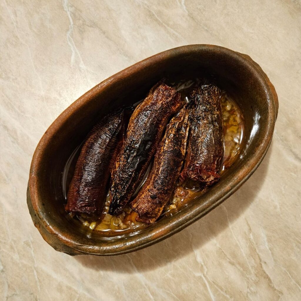 Served portion of Meatless Stuffed Dried Peppers in a small ceramic dish with a little cooking liquid.
