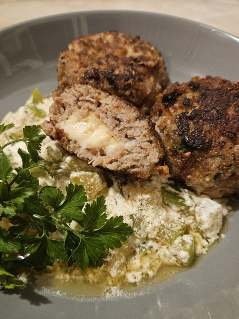 Close-up of Meat Patties Zucchini Cream served on a plate, with golden melted cheese and creamy zucchini cubes.