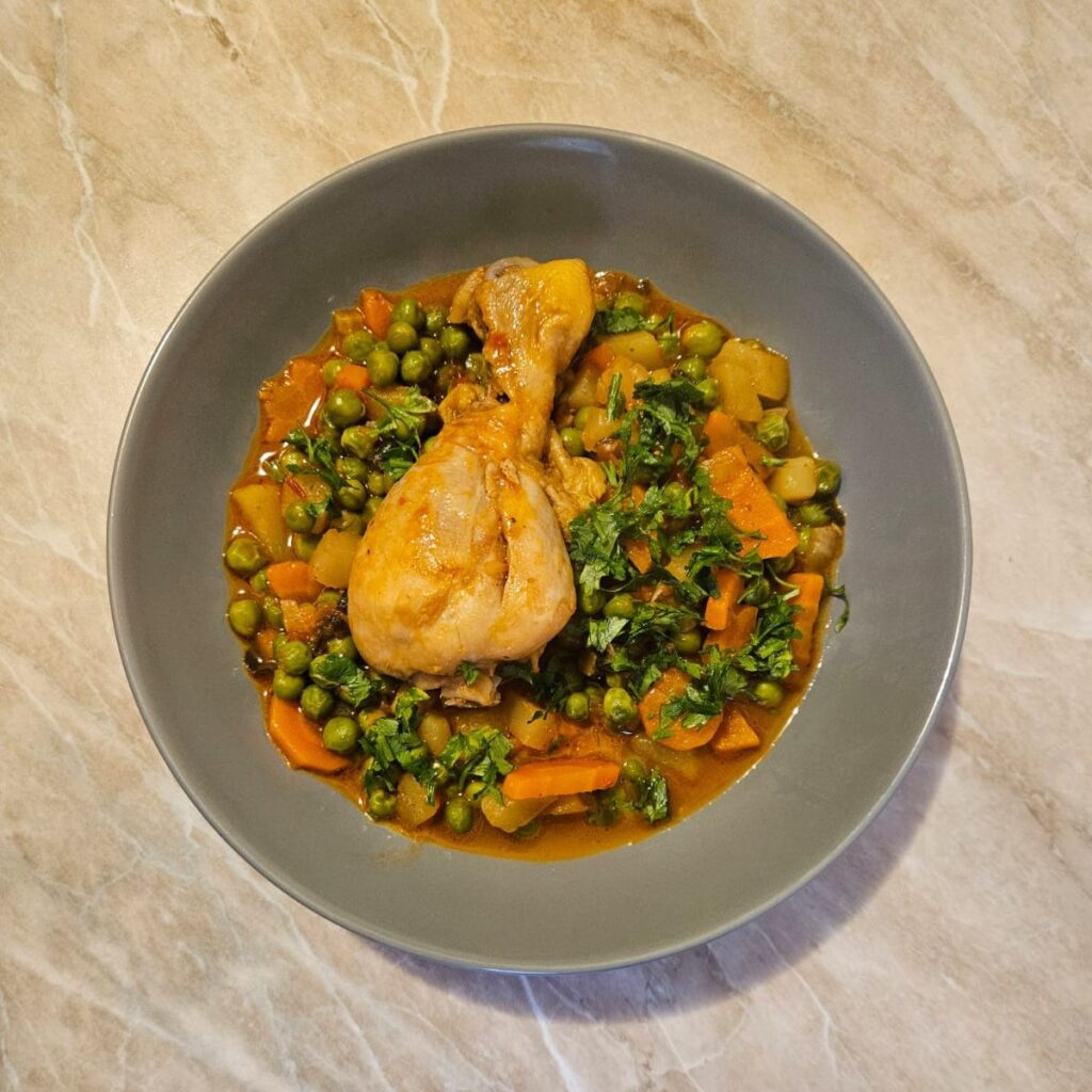 Served portion of Chicken Drumstick Pea Stew in a bowl with one chicken drumstick, peas, thick base, and freshly chopped parsley on top.