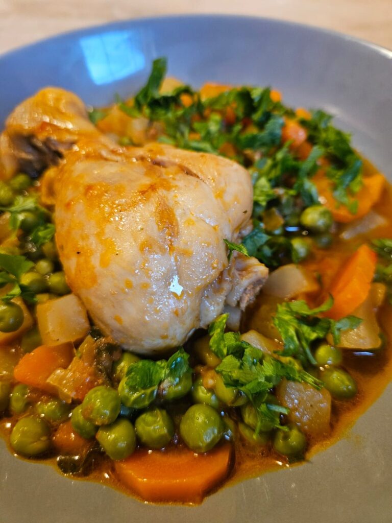 Close-up of a served bowl of chicken drumstick pea stew with visible peas, vegetables, and chicken drumstick.