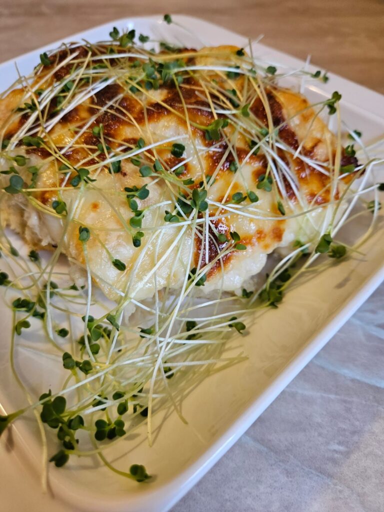 Close-up of baked cheesy bread cubes topped with fresh broccoli microgreens and melted cheese layers.