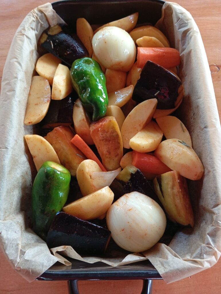 Seasoned vegetables spread in a baking tray and prepared for roasting.